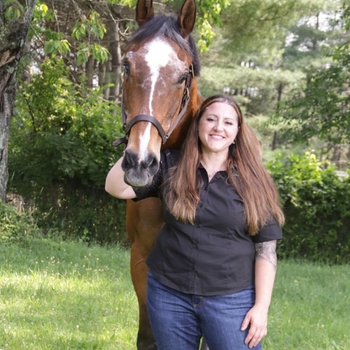 Kristen standing next to her horse on a clear day