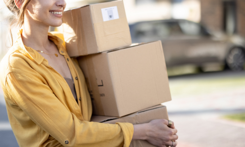 Woman in a yellow shirt carrying cardboard boxes to her home